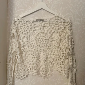 Vit spetsblus från by ESQ - Säljer en vacker vit spetsblus från by ESQ med ett unikt virkat mönster. Blusen har långa ärmar och en luftig design som ger en bohemisk känsla. Perfekt för att lägga till en romantisk touch till din outfit. 