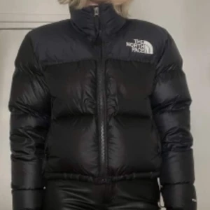 Svart pufferjacka från The North Face - Säljer en svart pufferjacka från The North Face. Jackan har en dragkedja framtill och är långärmad. Perfekt för kyligare väder med sin vadderade design.