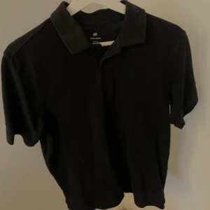 Svart pikétröja från H&M - Säljer en klassisk svart pikétröja från H&M. Tröjan har korta ärmar och en stilren krage. Perfekt för en avslappnad men ändå snygg look.
