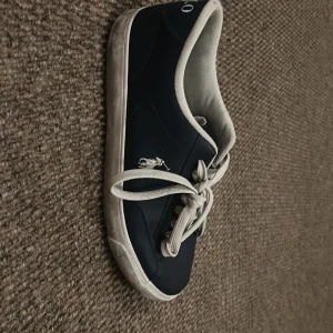 Marinblå sneakers från Polo - Snygga marinblå sneakers från Polo med vita snören och en vit sula. Skorna har en klassisk design med Polo-loggan på sidan. Perfekta för en avslappnad stil.