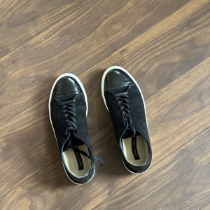 Sneaky Steve - Snygga svarta sneakers med ovandel i mocka och tå i skinn. De har en klassisk snörning och vit sula som ger en stilren look. Perfekta för en avslappnad stil.