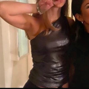 Svart glittrig oneshoulder topp - Snygg svart glittrig oneshoulder topp perfekt för en utekväll. Toppen har en tight passform och är tillverkad i ett glansigt material som ger en festlig look. Perfekt för att sticka ut på dansgolvet! 🖤✨