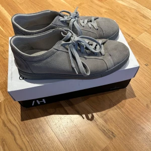 Grå sneakers från Selected Homme - Snygga grå sneakers i mocka från Selected Homme. De har en klassisk design med snörning och en bekväm passform. Perfekta för en stilren look. Använt skick men de är fortfarande i bra skick. För fler frågor skriv till mig! Box kommer med!