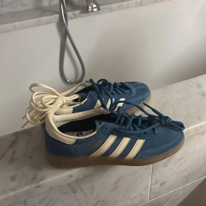Blå Adidas Samba sneakers - Snygga blå Adidas Samba sneakers med vita detaljer och klassiska tre ränder. Skorna har en gummisula och snörning i matchande blå färg. Perfekta för en stilren och sportig look. aldrig använda!! ingen förpackning för mamma slängde