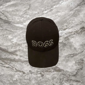 Svart keps från BOSS - Snygg svart keps från BOSS med broderad logga framtill. Perfekt för en stilren look. Justerbar passform för optimal komfort.