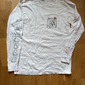 Vit långärmad tröja från Stüssy - Säljer en vit långärmad tröja från Stüssy med tryck på bröstet och ärmen. Tröjan har en avslappnad stil och är perfekt för en casual look. Tillverkad i Mexiko. Sliten i armhålan