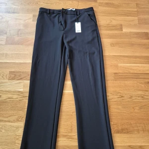 Svarta kostymbyxor - Eleganta svarta kostymbyxor med rak passform. Byxorna har en klassisk design med knappar och dragkedja i midjan. Perfekta för en stilren look.