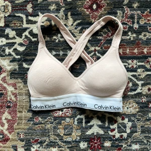 Rosa sport bh från Calvin Klein - Säljer en snygg rosa sport bh från Calvin Klein med korsade axelband och elastiskt band med logga. Perfekt för en avslappnad stil eller som basplagg. Superbekväm och stilren design! I mycket bra skick förutom lite nopprig, det syns på bilderna. Endast använt ett fåtal gånger 🩷