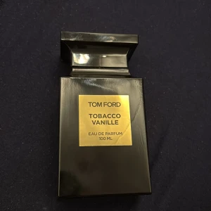 Tom Ford Tobacco Vanille Eau de Parfum - Säljer en lyxig Tom Ford Tobacco Vanille Eau de Parfum i en elegant svart flaska med guldetikett. Flaskan rymmer 100 ml och har en stilren design som utstrålar exklusivitet. Perfekt för den som älskar varma och kryddiga dofter med inslag av tobak och vanilj. Bara tyvärr ingen förpackning.