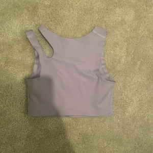 Ljuslila oneshoulder topp från Move - Säljer en stilren ljuslila oneshoulder topp från Move. Perfekt för träning eller en avslappnad dag. Toppen är ärmlös och har en modern design med en axelrem.