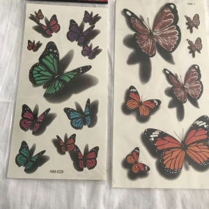Tatuering klistermärken med fjärilar och tribal mönster - Två ark med klistermärken. Ett ark med färgglada fjärilar i olika storlekar och färger som grön, lila och röd. Det andra arket har tribal mönster i svart och brunt, inklusive sol- och eldliknande former. Perfekt för tillfällig dekoration eller som inspiration för riktiga tatueringar. 50kr/2st /bild, sammafrakt 