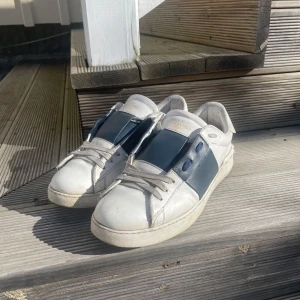 Valentino Garavani  - Snygga Valentino Garavani sneakers i vitt med blå detaljer. Använda men har ännu mycket kvar att ge. Låda finns. Skicket ca 7-8/10. Fler bilder eller funderingar skriv gärna. Priset kan diskuteras vid en snabb affär 