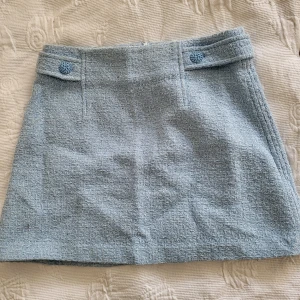 Ljusblå kjol från Zara - Säljer en söt ljusblå kjol från Zara med en texturerad yta och dekorativa knappar framtill. Kjolen har en kort längd och en stilren design som passar perfekt för vår och sommar. Perfekt för att skapa en chic look! 💙