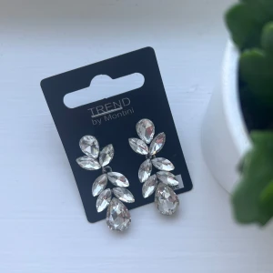 Glittriga örhängen från Montini - Snygga och glittriga örhängen från Montini. De har en elegant design med flera klara stenar i olika former som ger en lyxig känsla. Perfekta för att lysa upp vilken outfit som helst. Önskar du veta exakta mått? Tveka inte att höra av dig!