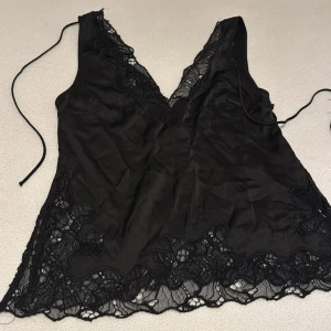 Svart linne från H&M - Snygg svart linne från H&M med spetsdetaljer längs kanterna och en djup v-ringning. Perfekt för en stilren look. 🖤