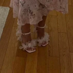 Rosa klackar med blommiga detaljer - Eleganta rosa klackar med blommiga detaljer och smala remmar. Perfekta för en somrig look med en touch av romantik. De har en fyrkantig tå och en justerbar rem runt ankeln.