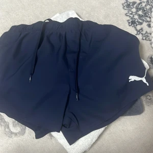 Mörkblå shorts från Puma - Snygga mörkblå shorts från Puma med elastisk midja och dragsko för justerbar passform. Perfekta för sportiga aktiviteter eller en avslappnad dag. Puma-loggan i vitt på benet ger en stilren touch.