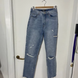 Blå jeans från Missguided - Snygga blå jeans från Missguided med slitna detaljer och hög midja. De har en klassisk femficksdesign och en knappgylf. Perfekta för en avslappnad stil med en modern twist.