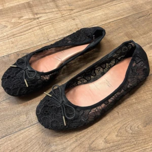 Svarta spetsballerinaskor med rosett - Eleganta svarta ballerinaskor i spets med en söt rosett framtill. Perfekta för en stilren look med en touch av romantik. Skorna har en mjuk insida och en diskret spetsig tå. Innesulan är 26cm. Sulan är sliten men inget jag märker när man har på sig dem! 