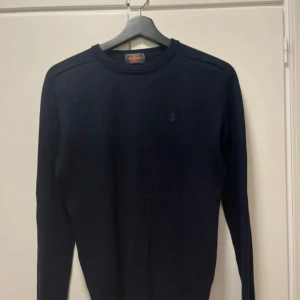 Mörkblå tröja från Morris - Säljer en stilren mörkblå tröja från Morris i 100% merinoull. Tröjan har en klassisk rund halsringning och långa ärmar. Perfekt för sommarkvällar och nu till våren. På bild 4 och 5 ser man att har tröjan två små hål i nacken och bröstet men det är inget man märker av men påverksr priset.