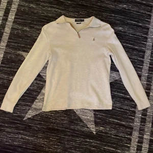 Vit långärmad tröja från Polo Ralph Lauren - Säljer en stilren vit långärmad tröja från Polo Ralph Lauren. Tröjan har en dragkedja vid halsen och är tillverkad i ett ribbat material. Perfekt för en avslappnad och snygg look.