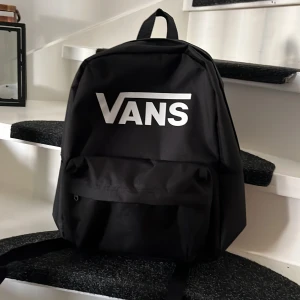 Svart ryggsäck från Vans - Säljer en stilren svart ryggsäck från Vans med deras ikoniska logga i vitt. Ryggsäcken har justerbara axelremmar och en praktisk dragkedja en stor och liten . Perfekt för att bära dina grejer med stil! 🖤