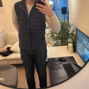 Mörkblå dunväst från Herno - Snygg mörkblå dunväst från Herno med dragkedja och knappar. Perfekt för lager-på-lager under kyliga dagar. Västen har en quiltad design och praktiska fickor. Tyvärr är den ett Litet hål i som kan ses på en av bilderna. Säljer den för jag ska köpa en ny men för den som vill är det nog lätt att laga. Ny pris ligger typ på 8-10k