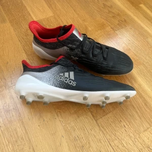 Svarta fotbollsskor från Adidas - Snygga svarta fotbollsskor från Adidas med vita och röda detaljer. Skorna har en strömlinjeformad design med snörning och dobbar för optimalt grepp på planen. Perfekta för fotbollsspelare som vill ha stil och funktionalitet.