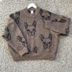 Brun stickad tröja med hundmotiv från C.W. - Säljer en brun stickad tröja från C.W. Carin Wester, med ett fint hundmotiv i svart. Tjock och mjuk alpackablandning. Längd 65 cm.  🐶