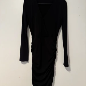 Svart omlottklänning - Klänning från bikbok, använd 1 gång. Klänningen har V ringning, långa ärmar och schrunch längst sidorna på kjolen. 
