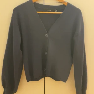 Svart kofta från vero Moda - Säljer en stilren svart kofta från Vero Moda. Den har en v-ringad design med knappar framtill och långa ärmar. Perfekt för lager-på-lager under kyligare dagar.