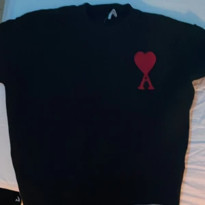 Ami Hoodie passar S/M - Säljer en stilren svart tröja från Ami Alexandre Mattiussi med ett rött hjärta och bokstaven A broderat på bröstet. Perfekt för en trendig look.