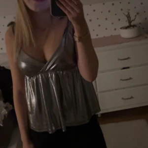 Silverfärgad glittrig linnetopp från Gina Tricot - Säljer en snygg silverfärgad glittrig linnetopp från kidsbrandstore. Den är i 170 men passar på mig som brukar ha                 xs/sToppen har en v-ringad design och tunna axelband, perfekt för en kväll ute. Den har en lös passform som ger en bekväm känsla.