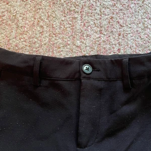 Svarta kostymbyxor - Snygga svarta kostymbyxor med knapp och dragkedja framtill. Byxorna har en klassisk design med hällor för bälte och diskreta bakfickor. Perfekta för en stilren look.