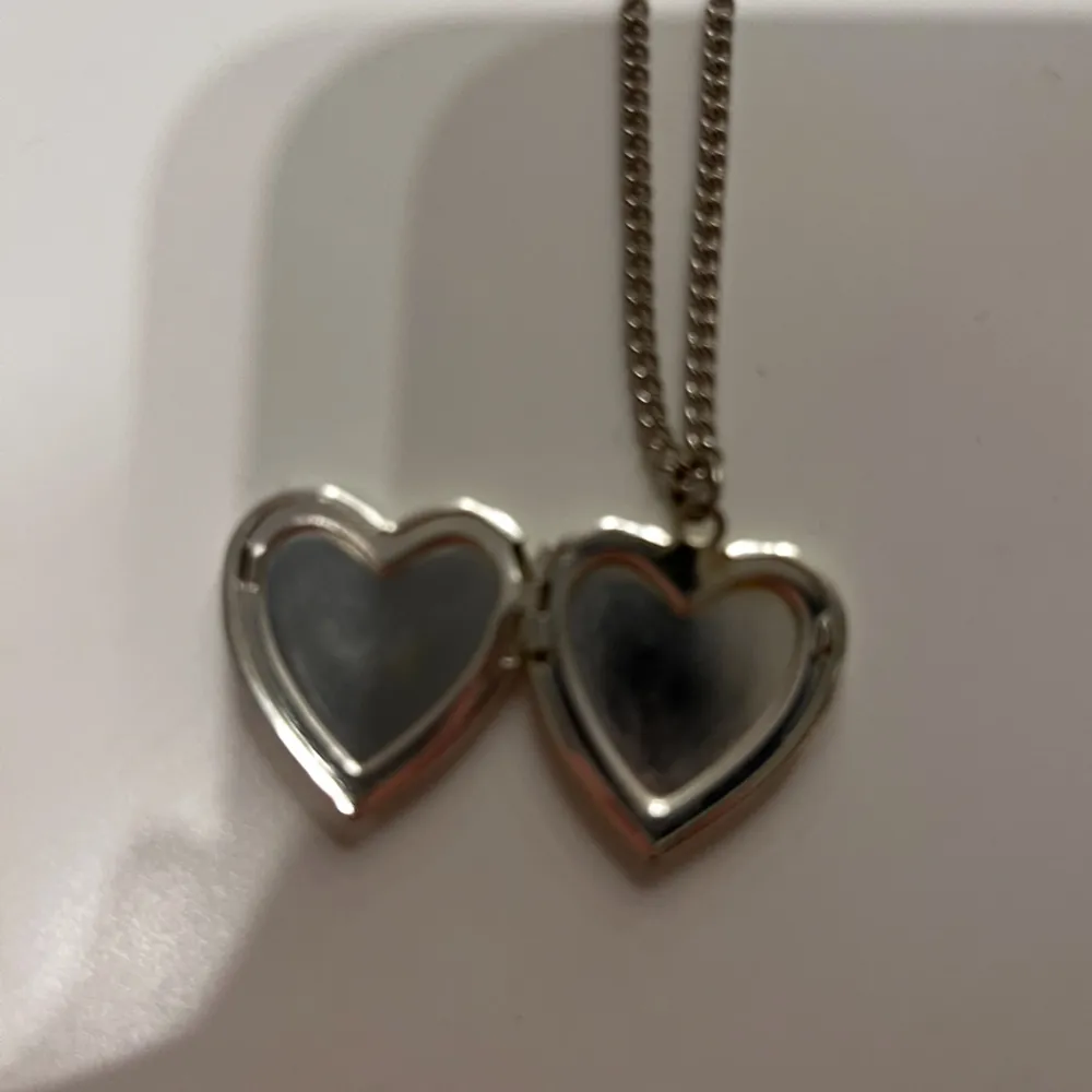 Charmigt halsband med en hjärtformad berlock som kan öppnas. Berlocken är glittrig i rött och har en silverfärgad kedja. Perfekt för att bära nära hjärtat.. Asusteet.