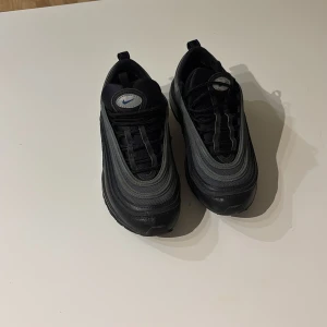 Nike air Max 97 - Snygga svarta Nike sneakers med en modern design och ikonisk logga på plösen. Skorna har en stilren look med svarta och gråa nyanser samt en bekväm passform. Perfekta för en sportig stil.
