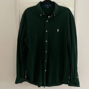 Grön långärmad skjorta från Ralph Lauren - Snygg grön långärmad skjorta från Ralph Lauren med klassisk krage och knappar framtill. Den har en broderad logotyp på bröstet och är perfekt för en stilren look. Passar bra till jeans.