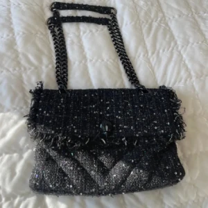 Svart paljettväska Kurt Geiger - Säljer denna superfina svarta axelväska från Kurt Geiger i glittrigt tyg med paljetter och grov textur. Säljer den eftersom jag köpt en ny liknade. Väskan har kedjerem med tygdetaljer, fransiga kanter och lockstängning. Köpte den från en tjej på Plick och hon köpte den för 2200kr men säljer denna för 1499kr. 