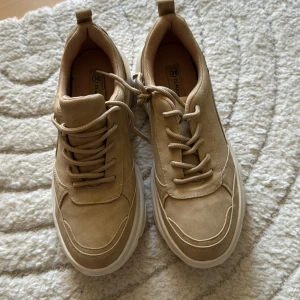 Beige chunky sneakers från Claudia Ghizzani - Chunky sneakers i beige mocka-look från Claudia Ghizzani. Skorna har tjock vit sula, rund tå och snörning framtill. Perfekta för dig som gillar en clean och trendig stil. Snygga detaljer och bekväm passform.