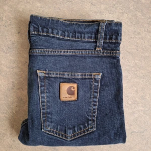 Carhartt Rebel Pants - Säljer ett par mörkblå Carhartt Rebel Pant jeans i storlek 31/34. Klassisk femficksmodell med snygga kontrastsömmar och Carhartt-logga på bakfickan. Jeansen är tillverkade i bomull med lite stretch för skön passform.