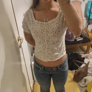 Blommig croppad topp med fyrkantig ringning - Supersöt croppad topp med blommigt mönster i ljusgrönt och vitt. Toppen har en fyrkantig ringning och korta ärmar, perfekt att matcha med jeans eller kjol. Lätt och skön att bära under varmare dagar.