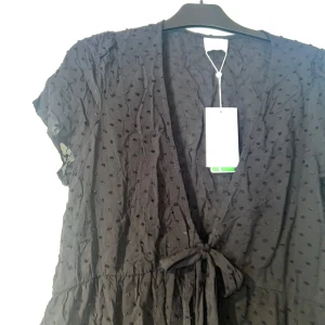 Svart kofta med knyt från Vila - Supersöt svart kofta från Vila med diskreta prickar i tyget, v-ringning och knyt i midjan. Koftan har korta ärmar och luftig passform, perfekt för en trendig look. Materialet känns lätt och flowy. Aldrig använd. Nypris 399kr. Kan justera storlek. Passar allt från S-2XL