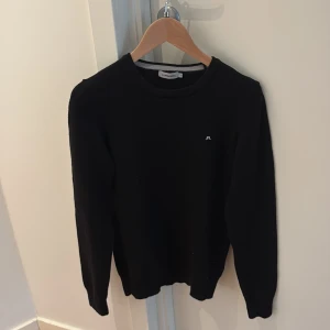 Svart stickad tröja från J.Lindeberg - Svart stickad tröja från J.Lindeberg i storlek S men passar mer som xs . Klassisk rund halsringning och diskret broderad logga på bröstet. Perfekt basic-plagg med lång ärm och mjuk känsla, passar till allt och är enkel att matcha. 