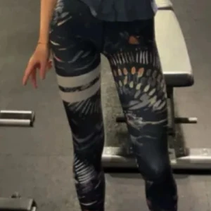 Stronger leggings med mönster - Snygga svarta leggings från Stronger med färgstarkt abstrakt mönster i vitt, orange och grått. Hög midja med logotyp i midjebandet och två vita ränder på ena benet. Perfekta för gymmet eller träning, sitter tight och bekvämt.