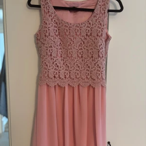 Rosa spetsklänning från Dry Lake - Supersöt rosa kortklänning från Dry Lake med vacker spets upptill och slät, lätt utsvängd kjol. Ärmlös modell med rund halsringning och fina detaljer i spetsen. Perfekt för dig som vill ha en feminin och romantisk look.