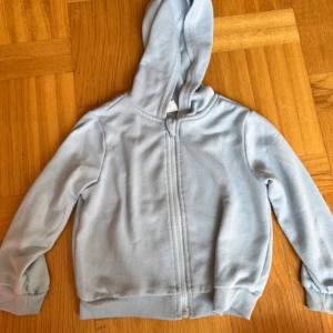 Ljusblå hoodiejacka från Shein 2-3 år - Mysig ljusblå hoodiejacka från Shein i mjuk bomullsmix. Jackan har dragkedja framtill, huva och ribbade muddar vid ärmslut och nederkant. Perfekt för chill dagar eller när du vill ha något enkelt och bekvämt på dig.