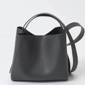 Svart stilren axelväska i skinn - Minimalistisk svart axelväska i slätt skinn med både handtag och lång axelrem. Väskan har en boxig form och passar perfekt för dig som gillar enkel och clean design. Rymmer allt du behöver till vardagen och är lätt att matcha med olika outfits.