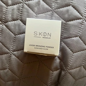 SKON Loose Bronzing Powder - Loose Bronzing Powder från SKON Makeup i nyansen Sunkissed Glow. Ger en naturlig solkysst look med ett fint glow. Perfekt för att framhäva ansiktskonturer och skapa värme i ansiktet. Kommer i en stilren, ljus förpackning.