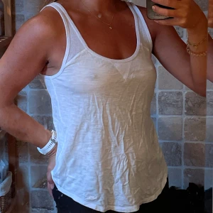 Vit linnetopp från Hollister XS - Säljer en vit linnetopp från Hollister i storlek XS. Toppen har breda axelband, rundad halsringning och en liten broderad logga nertill. Materialet är mjukt och tunt bomullstyg, perfekt för varma dagar.