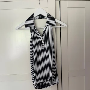 Randig linnetopp från Abercrombie & Fitch - Svartvit randig linnetopp från Abercrombie & Fitch med krage och v-ringning. Toppen är ärmlös och har två dekorativa knappar framtill.